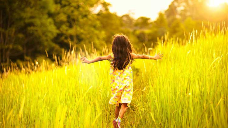 Back of young girl running in field of long grass.