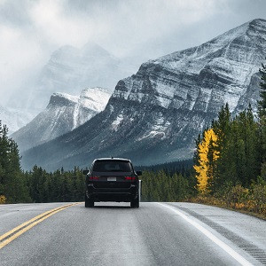 Car driving in the woods with a mountain in the background