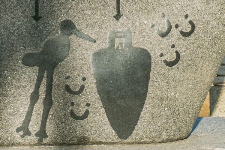 Photo of the Petroglyphs on the residential school monument that includes inverted moose tracks near a representation of a dark force, with a crane nearby.