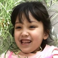 A young child wearing a pink shirt lies outdoors near grass and a paved surface.