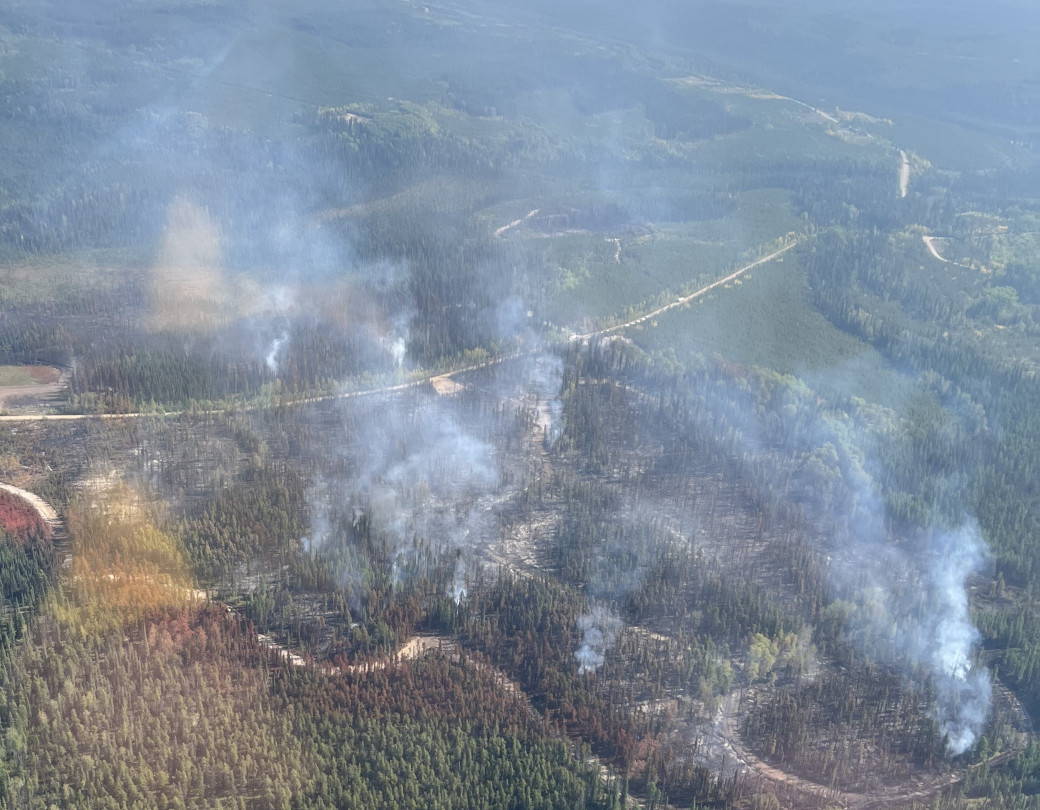 An areal shot of wildfire GWF111 in a heavily forested area. Smoke emits from the trees with a few dirt roads separating the trees.
