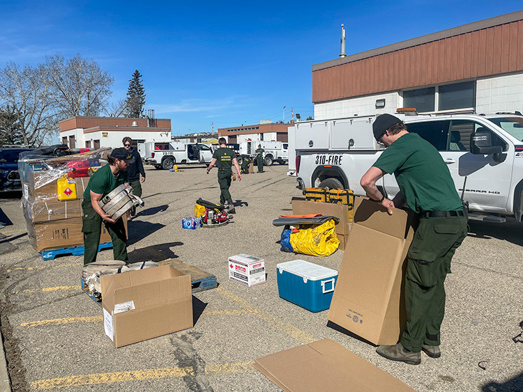 Crew members in green shirts organize firefighting equipment in a parking lot with fire‑marked trucks and supplies around them.