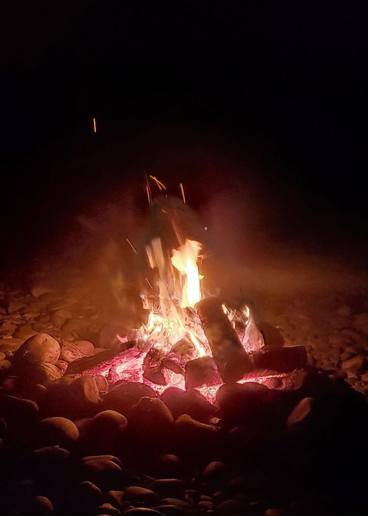 The red glow of a campfire in the night. Embers are popping up above the flames.