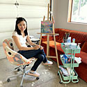 Aeris sits in a chair next to her artwork and smiles.