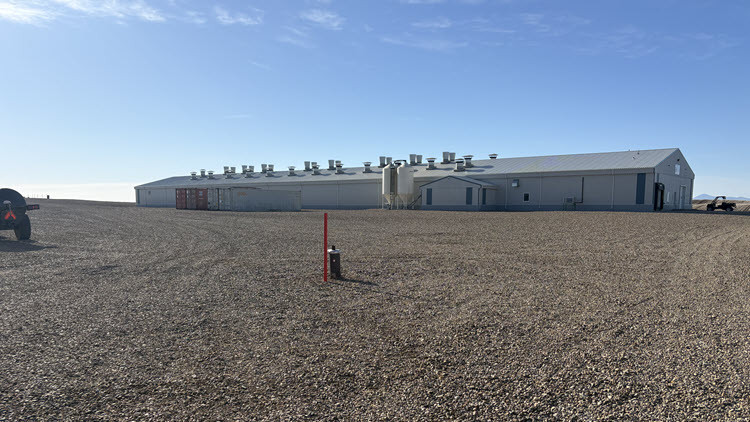 Water well monitoring equipment in the dirt ground; long white building in the background