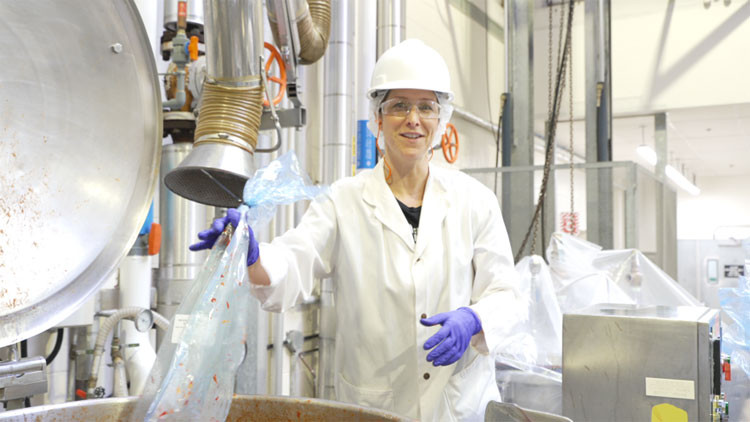 A person wearing a lab coat, hard hat and safety glasses working in  the food centre