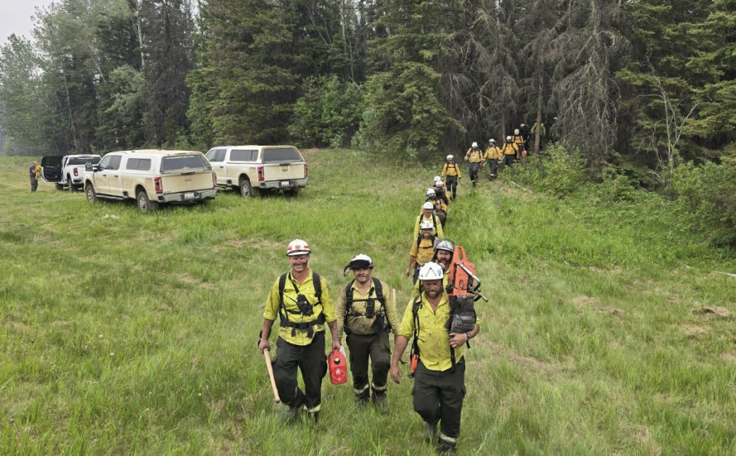 A line of firefighters make their way out of the forest. They are covered in ash and dirt after a long days work