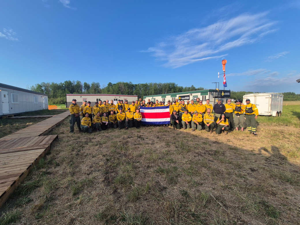 A large group of firefighters poses for a photo. The Costa Rican flag is held high in front.
