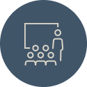 Icon of a classroom with a teacher at the front and students seated at the back of the classroom.