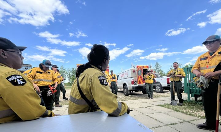 With a backdrop of a blue sky and a few clouds, a group of wildland firefighters is receiving a briefing.