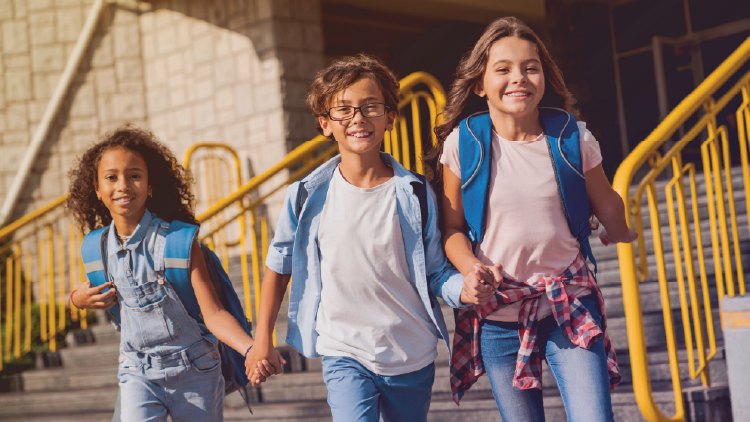 A boy and three girls holding hands walking down the steps of a school.