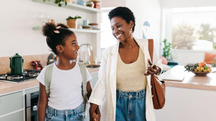 Adult and child holding hands in a bright, modern kitchen with a countertop, plants, and household items visible in the background.