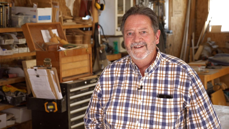 Mick sits in his woodshop, smiling.
