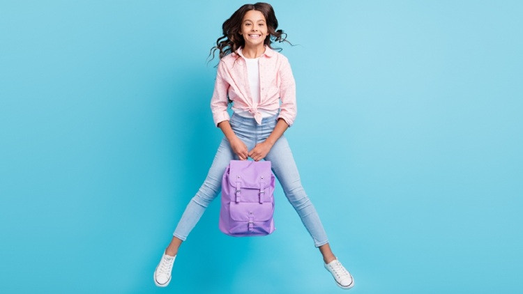 Student in mid-air holding a backpack against a blue background