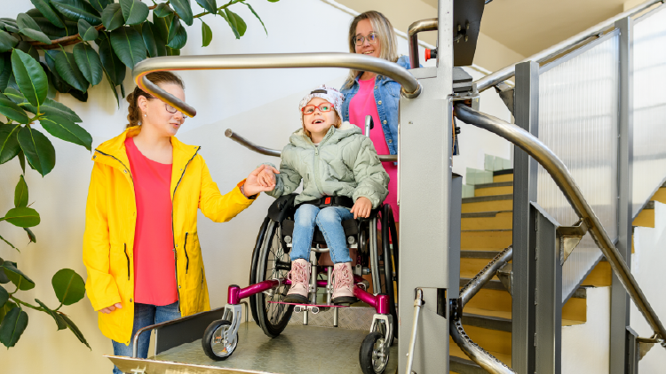 Child in a wheelchair on a ramp for climbing stairs with two women beside her