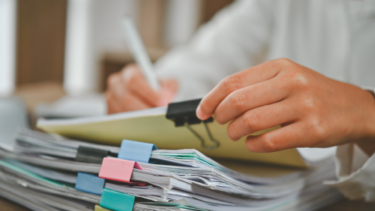 Hand holding a stack of files held together with a bullnose clip with more papers in a stack underneath