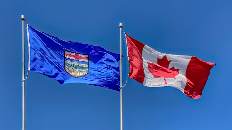 Alberta and Canada flags flying in the wind with the blue sky in the background
