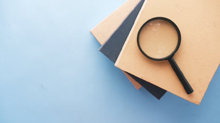 Magnifying glass on a stack of three books on a light blue background