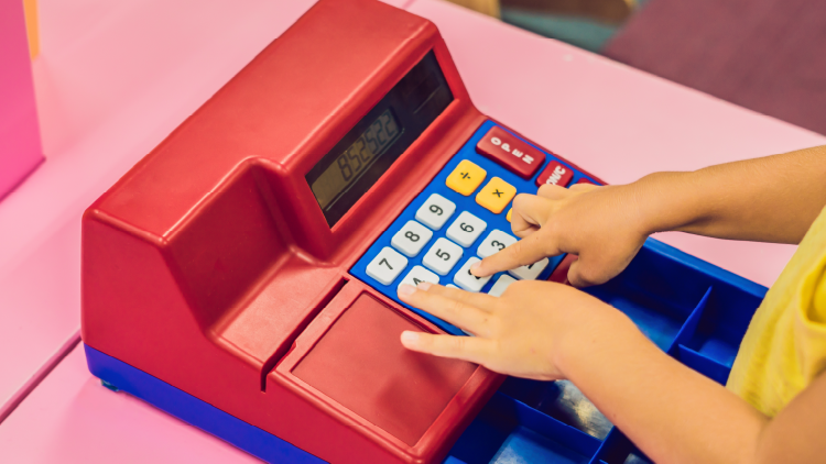 Close up of a young person's hands using a red toy cash register