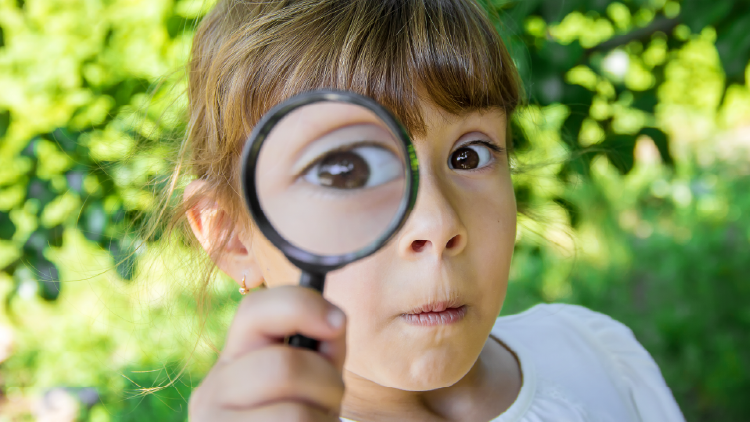 Young girl holding a magnifying glass up to her right eye