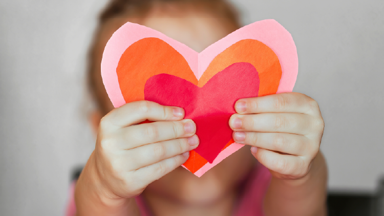 Close up of a child holding a multi-coloured construction paper heart