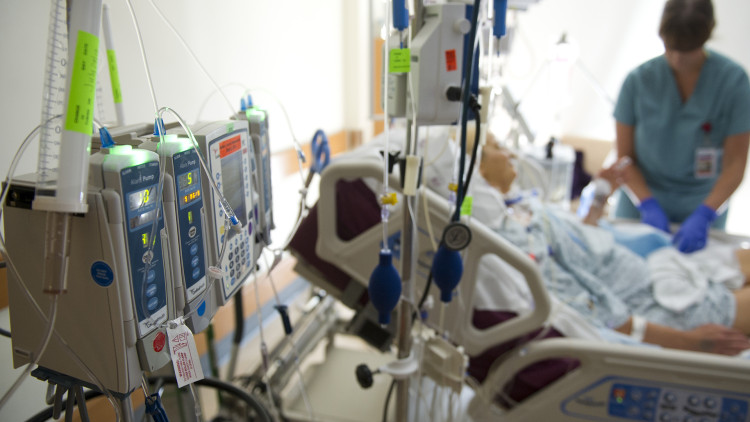 Image of a medical bed in a hospital with medical equipment and a hospital staff member standing next to the bed.