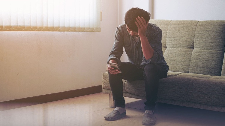 Man sitting on couch with head in hands looking at cellphone