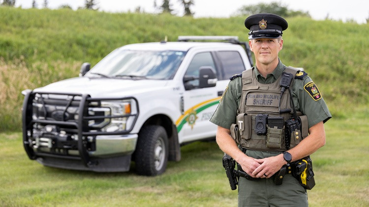 Male fish and wildlife officer standing in front of enforcement truck in a green field of grass
