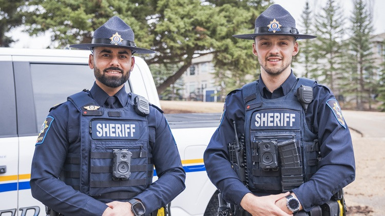 Two sheriffs standing outside next to an enforcement vehicle