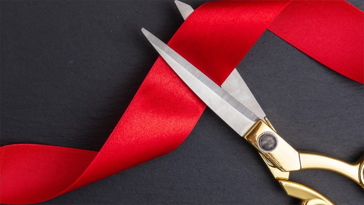 Gold scissors cut red tape laying on a black table.