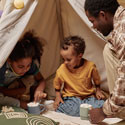 A dad plays with his two kids in a sheet tent in their living room.