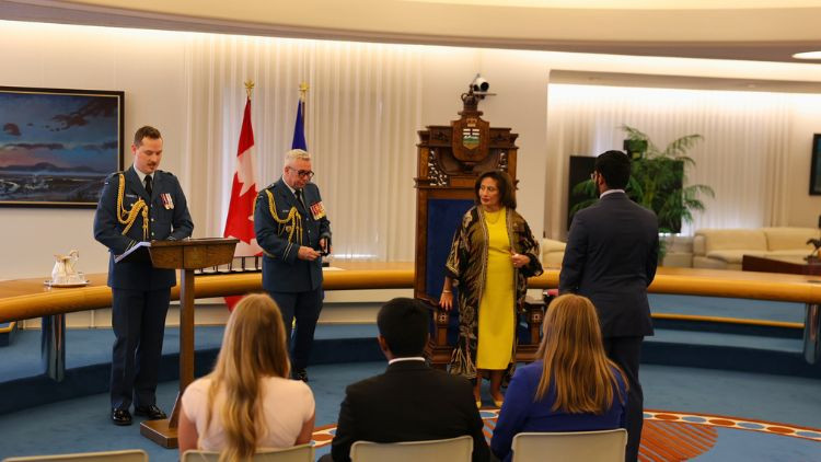 Award presentation ceremony in a formal chamber with attendees seated in the foreground and Canadian and Alberta flags in the background.