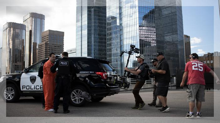 Film crew and characters next to a police suv