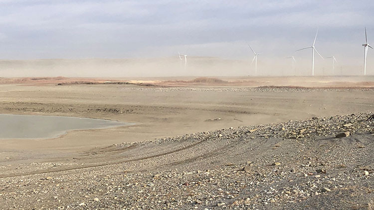 Oldman River Dam Provincial Recreation Area - water surrounded by rocks and dirt, wind turbines in the distance