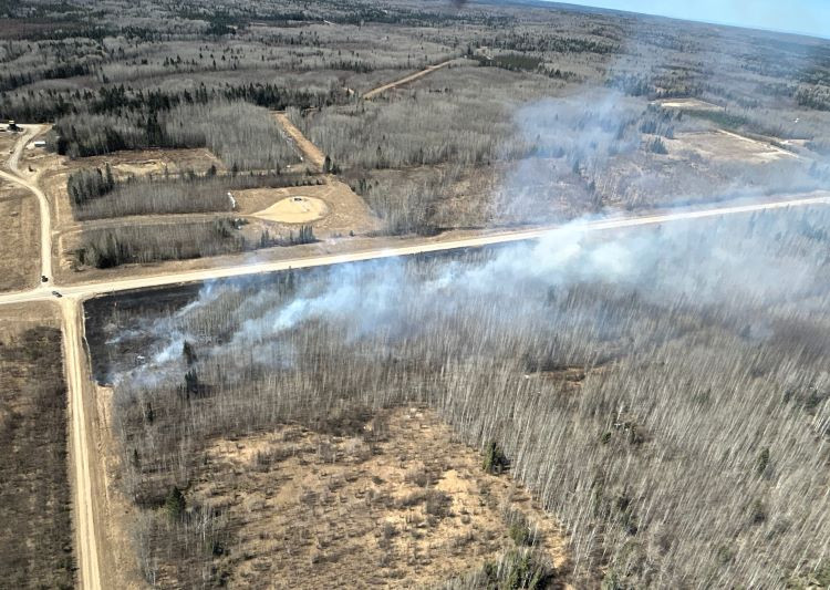 A wildfire is burning alongside the highway, mostly grass is burning and not into the trees.