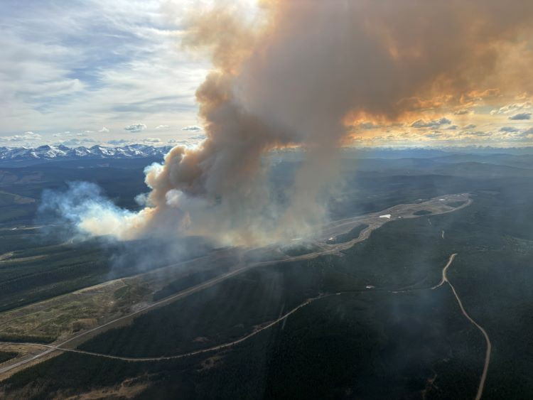 Smoke from the wildfire nearing a clearing with mountains in the background.