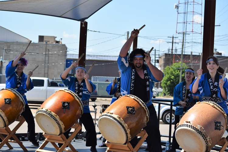 4 members of a Japanese drumming group perform on stage outside.