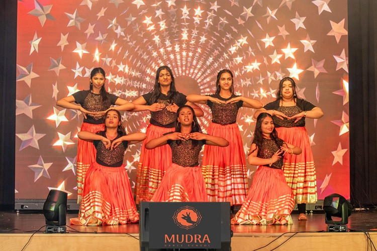 Dance group performs on a brightly lit stage.