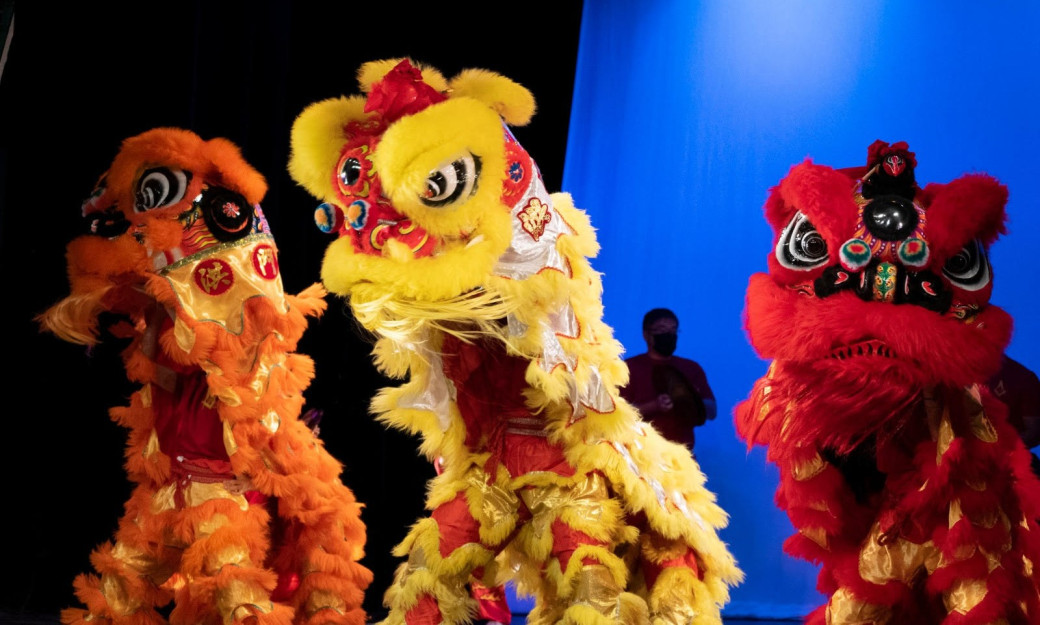 Three Lion Dance performers move on stage in red, orange and yellow costumes.