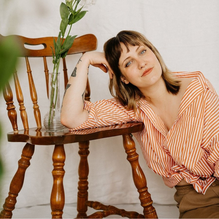 Mallory Chipman is sitting on the floor leaning against a chair. A flower in a vase sits on the chair.