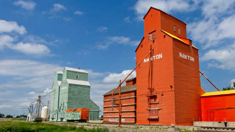 An old grain station in Nanton Alberta. An orange grain building in the foreground with blue, grey buildings in the background.