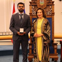 Award recipient Baber A. receives a medal during a presentation ceremony in the Alberta Legislature chamber.