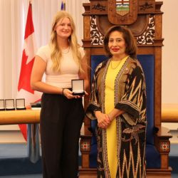 Award recipient Kate H. receives a medal during a presentation ceremony in the Alberta Legislature chamber.