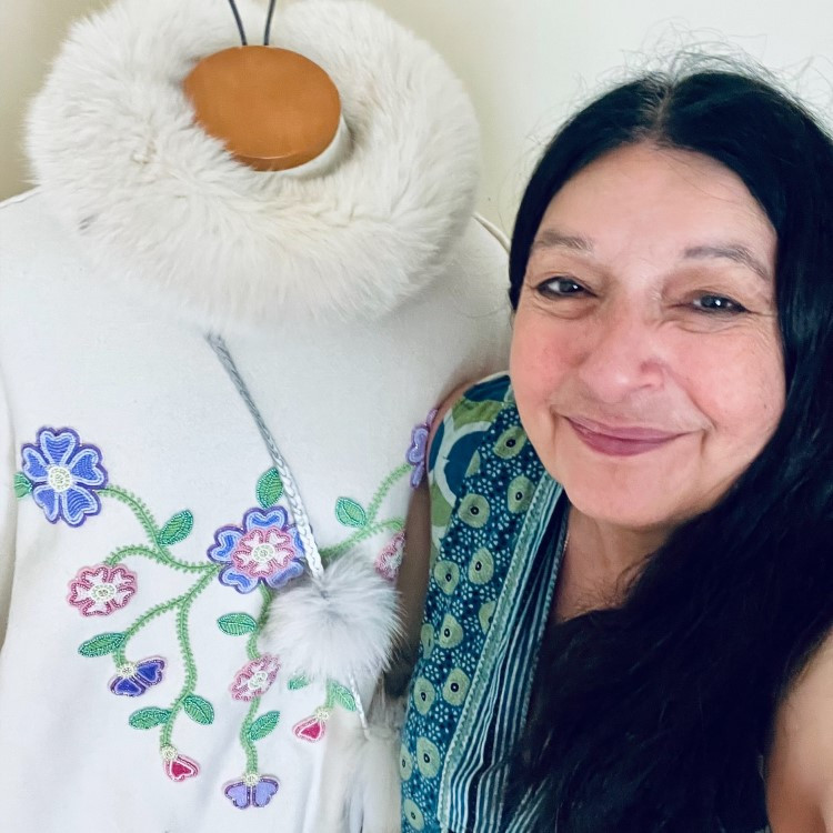 Sharon stands next to her beadwork on a white coat.