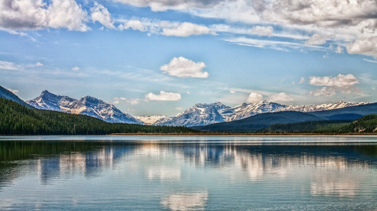 Lanscape featuring mountain and forest reflecting on the clear waters of a lake.
