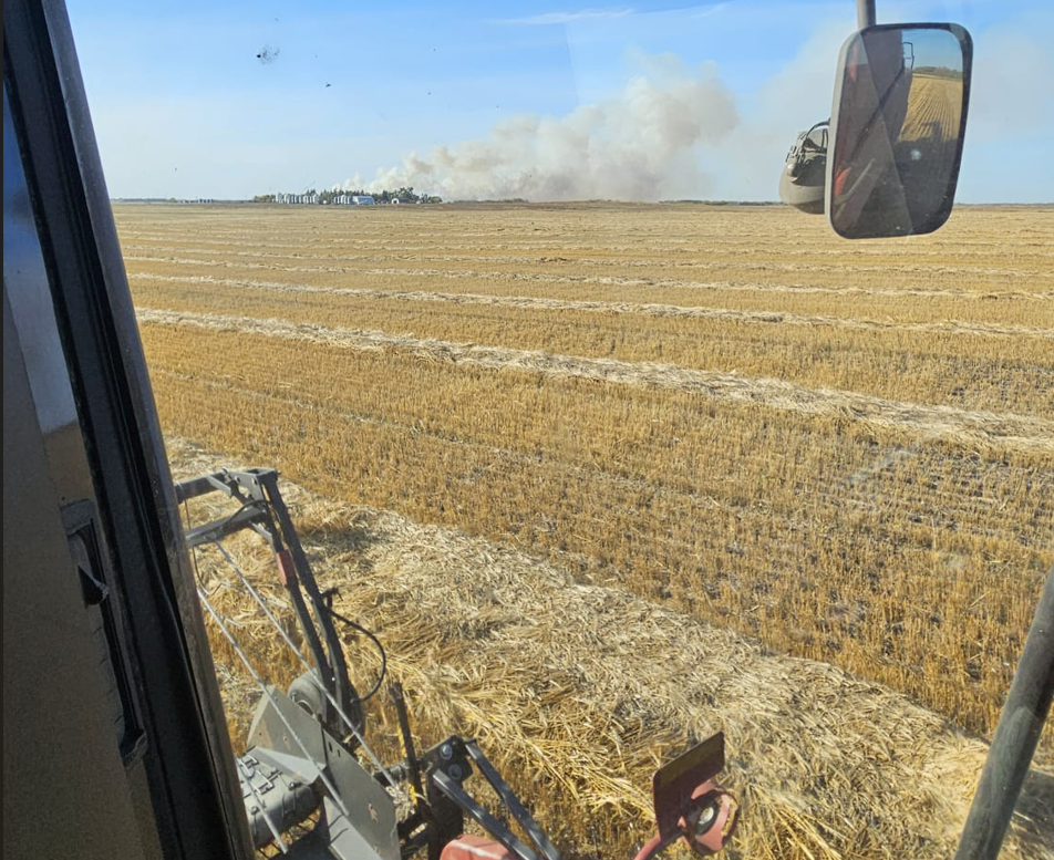A crop fire burns in the distance from the window of a combine harvester