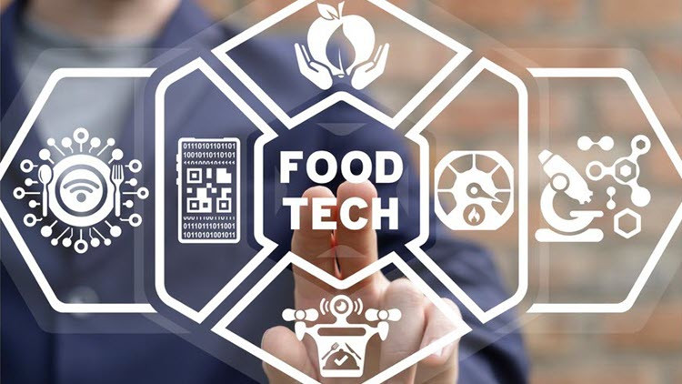 Person in a blue jacket and grey shirt touching a clear screen with two fingers - images and text on screen: Food Tech