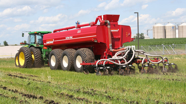 Green tractor pulling a red machine spreading manure on crops in a field