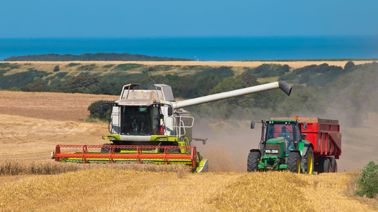 White, orange and green tractor emptying harvested crops into a green and red combine