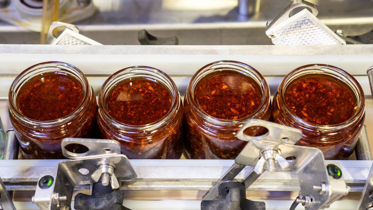 A person in a lab coat, face mask and hard hat scooping into a bin at the food centre